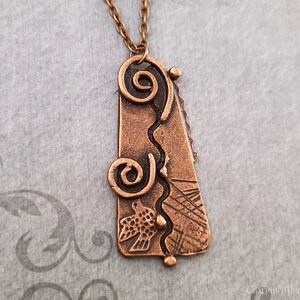 May include: A copper pendant necklace with a textured, abstract design featuring swirls, lines, and a bird. The pendant is attached to a copper chain.