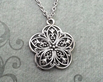 May include: Silver necklace with a delicate, ornate flower pendant. The pendant has a filigree design with intricate details.