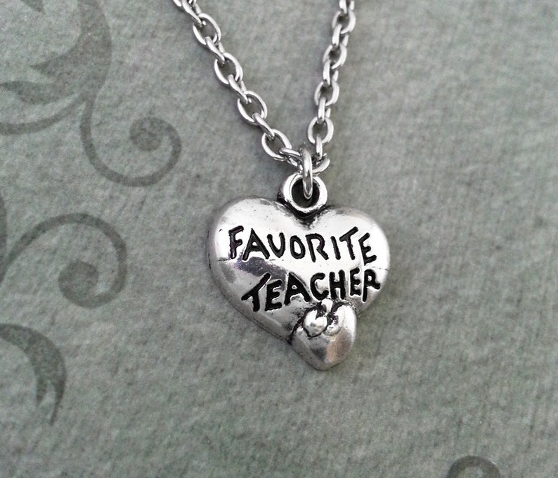 Op de afbeelding: Een zilveren ketting met een hartvormige hanger waarop "Favoriete Leraar" staat.