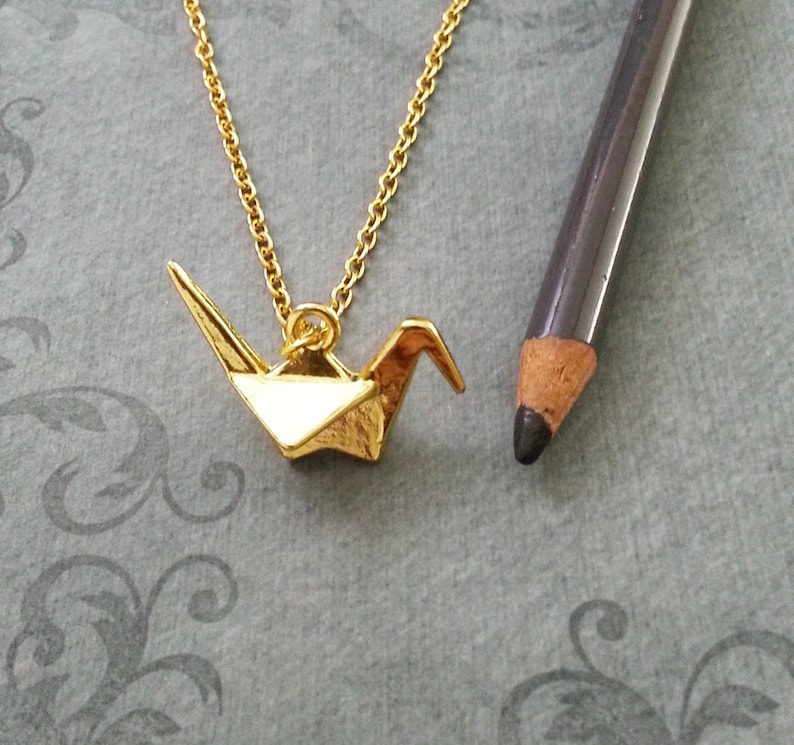 May include: A gold chain necklace with a gold origami crane pendant.