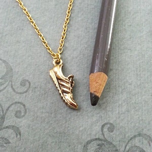 May include: A gold necklace with a small gold shoe charm. The shoe charm is a detailed replica of a running shoe.