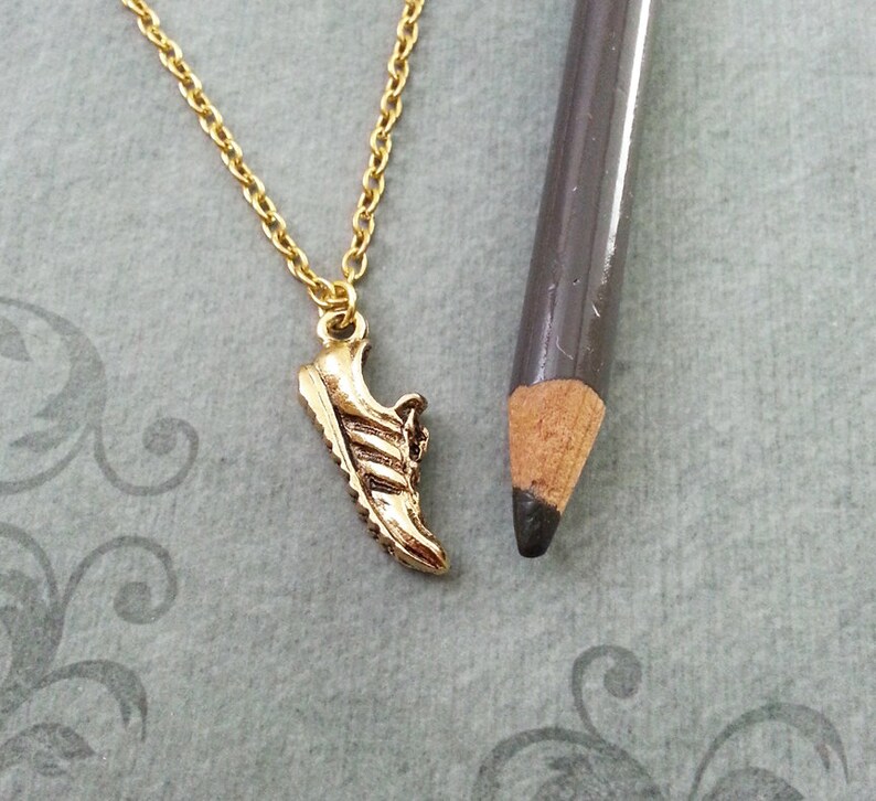 May include: A gold necklace with a small gold shoe charm. The shoe charm is a detailed replica of a running shoe.