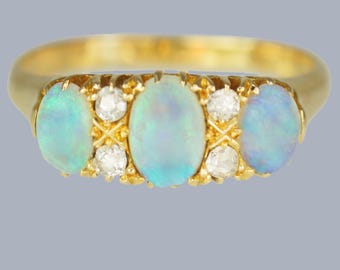 May include: A gold ring featuring three oval opals and four small diamonds. The opals have a pale blue color, and the diamonds are set between the opals. The ring has a classic design.