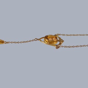 May include: A gold necklace with a teardrop-shaped pendant and a larger oval-shaped pendant with a gold setting. The oval pendant has a yellow gemstone in the center.