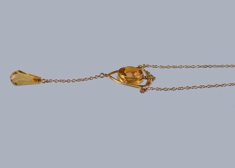 May include: A gold necklace with a teardrop-shaped pendant and a larger oval-shaped pendant with a gold setting. The oval pendant has a yellow gemstone in the center.
