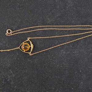 May include: A gold necklace with a teardrop-shaped pendant and a triangular pendant with a round, orange gemstone.