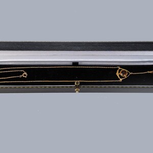 May include: A gold necklace with a pendant featuring a round, dark brown stone set in a delicate, geometric design. The necklace is displayed in a black velvet jewelry box.