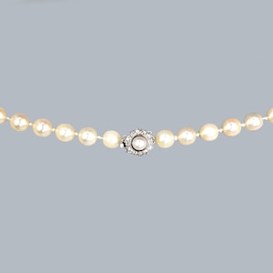 May include: A pearl necklace with a silver clasp featuring a small pearl surrounded by diamonds.