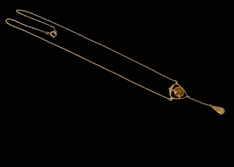 May include: A gold chain necklace with a teardrop pendant and a geometric design featuring a round, yellow gemstone.