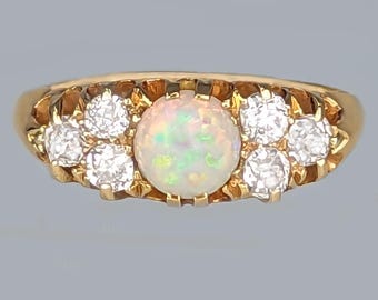 May include: A gold ring featuring a central opal stone surrounded by six smaller, clear gemstones. The ring has a classic design with a polished gold band and intricate detailing around the stones. The opal displays a play of color.