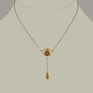 May include: A gold necklace with a teardrop pendant and a round amber stone set in a triangular frame.