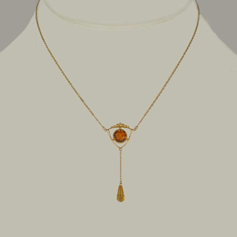 May include: A gold necklace with a teardrop pendant and a round amber stone set in a triangular frame.