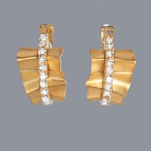 May include: A pair of gold-colored earrings with a unique design. Each earring features a textured, fan-like shape with a vertical row of sparkling white stones. The earrings have a clip-on style.
