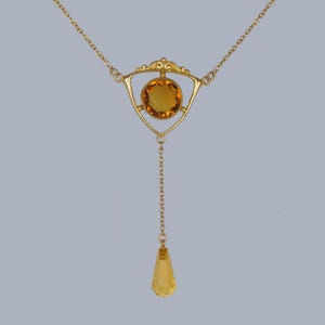 May include: A gold necklace with a teardrop-shaped pendant and a triangular centerpiece featuring a round, amber-colored gemstone.