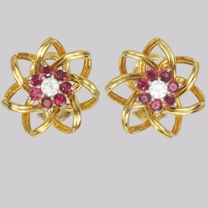 Può includere: Un paio di orecchini d'oro con un design a forma di fiore. Gli orecchini sono incastonati con rubini rossi e un singolo diamante al centro di ogni fiore.