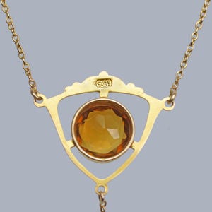May include: A gold necklace with a triangular pendant featuring a large, faceted amber-colored gemstone. The pendant is marked with the letters "9CF".