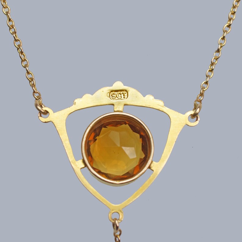 May include: A gold necklace with a triangular pendant featuring a large, faceted amber-colored gemstone. The pendant is marked with the letters "9CF".