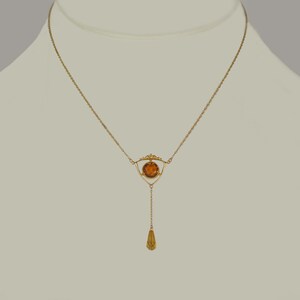 May include: A gold necklace with a teardrop pendant and a geometric design featuring a round amber stone.