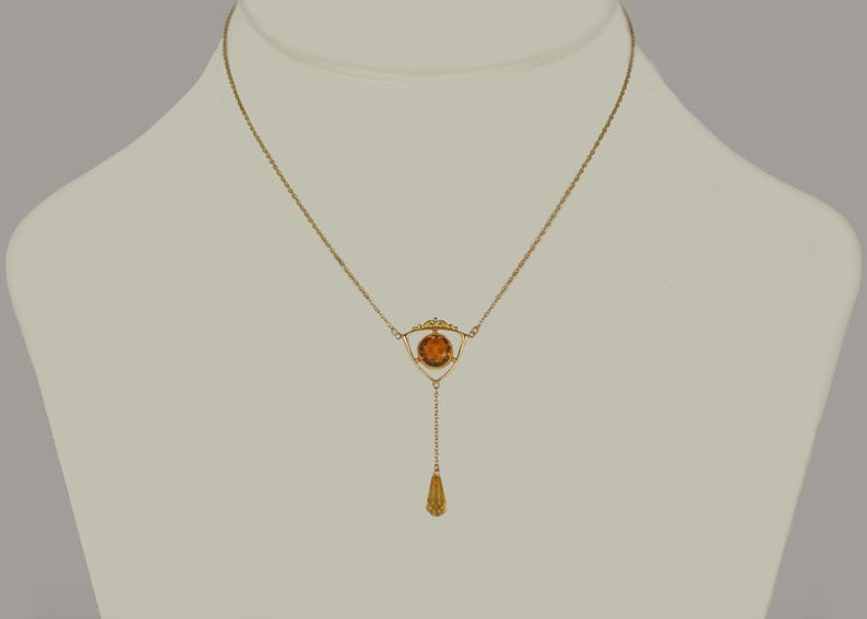 May include: A gold necklace with a teardrop pendant and a geometric design featuring a round amber stone.