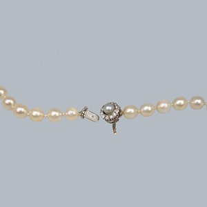 May include: A white pearl necklace with a silver clasp featuring a pearl surrounded by small diamonds.