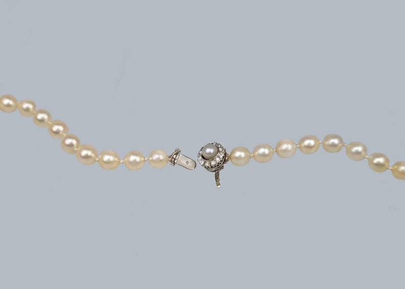 May include: A white pearl necklace with a silver clasp featuring a pearl surrounded by small diamonds.