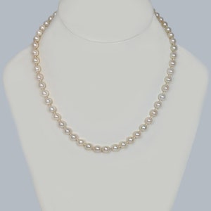 May include: A strand of white pearl beads on a white display stand. The pearls are round and smooth.