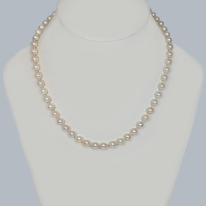 May include: A strand of white pearl beads on a white display stand. The pearls are round and smooth.
