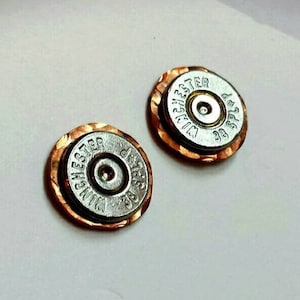 May include: A pair of copper and silver earrings featuring a round, textured copper base with a silver bullet casing in the centre. The bullet casing has the text "WINCHESTER 38 SPECIAL" printed on it.