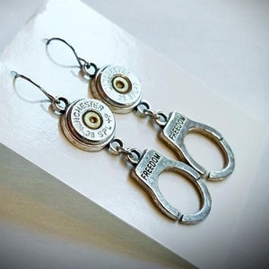 May include: Silver earrings with a bullet casing charm and a silver charm that says "FREEDOM".