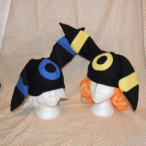 May include: Two black felt hats with yellow and blue accents. The hats are shaped like the Pokemon,  Eevee's evolutions,  Umbreon and Espeon.