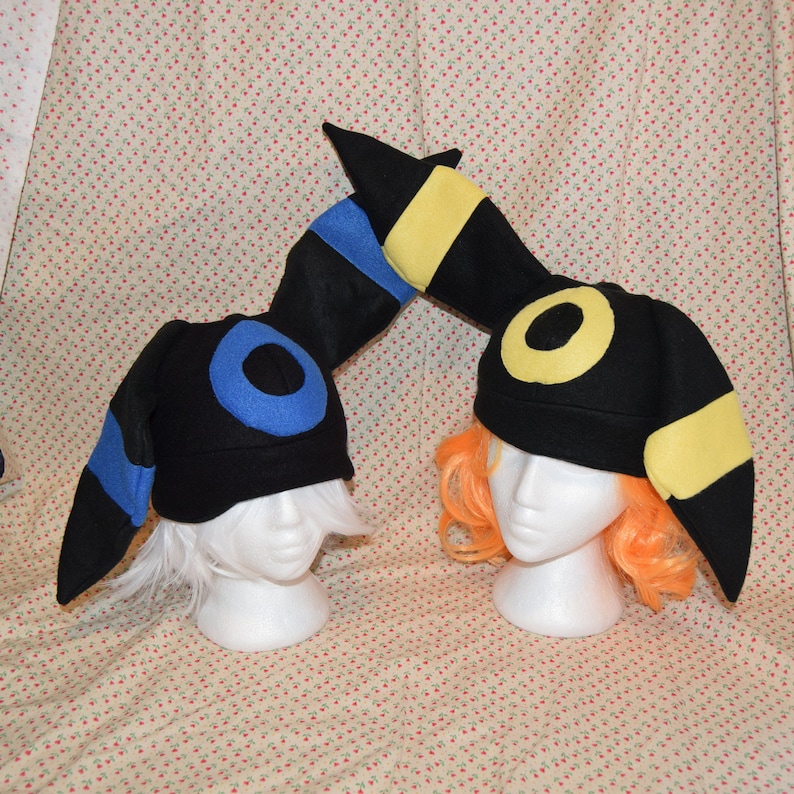 May include: Two black felt hats with yellow and blue accents. The hats are shaped like the Pokemon,  Eevee's evolutions,  Umbreon and Espeon.
