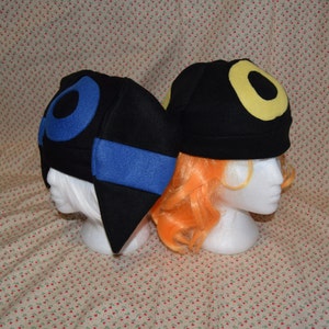May include: Two black fleece hats with different colored symbols. One hat has a blue symbol and the other has a yellow symbol.