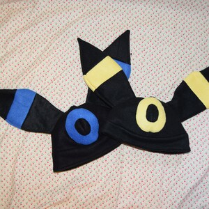 May include: Two black felt hats shaped like the Pokemon character, Umbreon. The hats have yellow and blue accents on the ears.