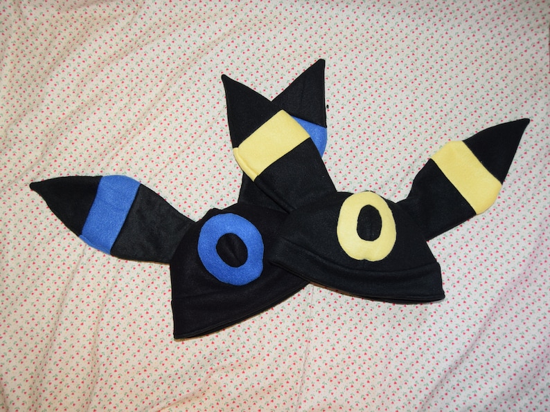 May include: Two black felt hats shaped like the Pokemon character, Umbreon. The hats have yellow and blue accents on the ears.