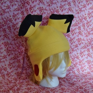 May include: Yellow fleece hat with black ears and red accents. The hat is shaped like a cartoon character with large ears.
