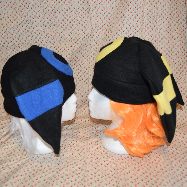 May include: Two black fleece hats with blue and yellow ear flaps. The hats are designed to look like the Pokemon characters,  Latias and Latios.