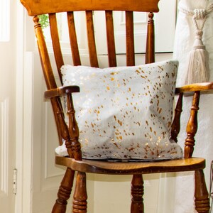 Peut inclure: Une chaise berçante en bois avec un coussin à motifs blancs et dorés. La chaise a un dossier haut et un siège incurvé.