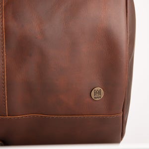 May include: A brown leather bag with a small metal logo that says "MAHI" on it.
