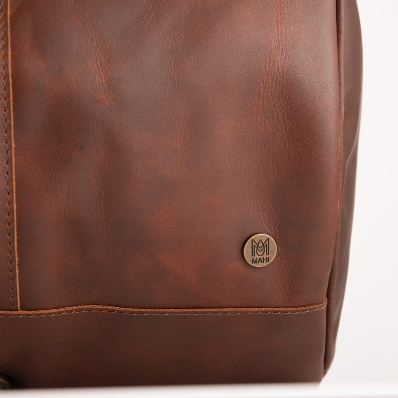 May include: A brown leather bag with a small metal logo that says "MAHI" on it.
