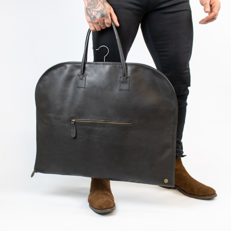 May include: A black leather garment bag with a zippered pocket and a hanging hook. The bag is large enough to hold a suit or dress.