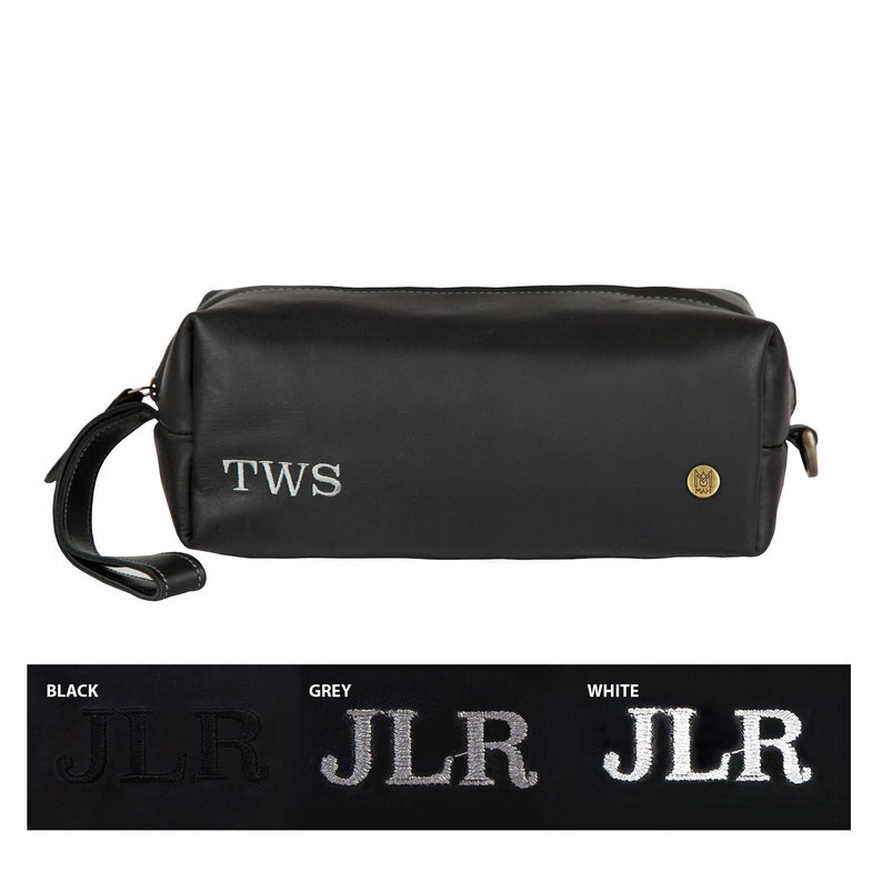 Puede incluir: Bolsa de aseo de viaje de cuero negro con cierre de cremallera y asa superior. La bolsa tiene las iniciales "TWS" bordadas en hilo plateado en la parte delantera.