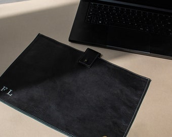 May include: Black leather laptop sleeve with a blue stitch detail and a gold logo. The sleeve has a flap closure with a snap button and the initials "FL" are embroidered on the front.