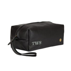 Puede incluir: Bolsa de viaje de cuero negro con cierre de cremallera y asa superior. La bolsa tiene una inscripci&oacute;n monograma que dice "TWS".