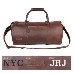 May include: Brown leather duffel bag with a shoulder strap and top handles. The bag has a zippered pocket on the front and the text "LAX" is embroidered on the side.