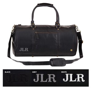 May include: Black leather duffel bag with a top handle and a shoulder strap. The bag has a zippered pocket on the front and a gold metal buckle on the side. The initials "JLR" are embroidered on the front of the bag in white.