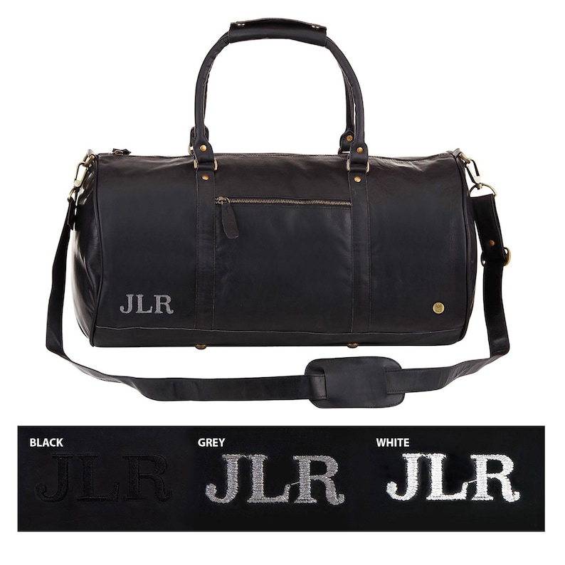 May include: Black leather duffel bag with a top handle and a shoulder strap. The bag has a zippered pocket on the front and a gold metal buckle on the side. The initials "JLR" are embroidered on the front of the bag in white.