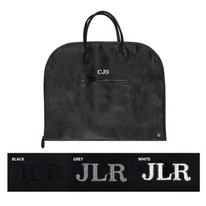 May include: Black garment bag with a zippered pocket and two handles. The bag has the initials "CJS" embroidered on the front. The bag is shown with three different monogram options: black, grey, and white.