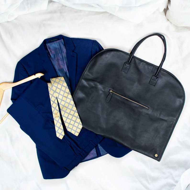 May include: A navy blue suit jacket with a yellow and white patterned tie, and a black leather garment bag with a zippered pocket.