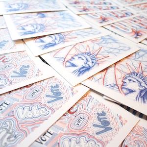 May include: A stack of white cards with a blue and red design featuring the word "Vote" and a drawing of the Statue of Liberty.