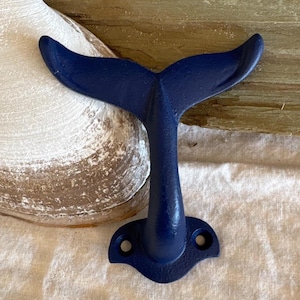 May include: A navy blue metal whale tail hook. The hook is designed to look like a whale tail and has two holes on the bottom for hanging items.